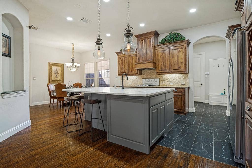 1250 Packsaddle Trail, Prosper, TX 75078 Kitchen featuring an island with a light-toned countertop, wood-finish flooring, and dark wood cabinetry