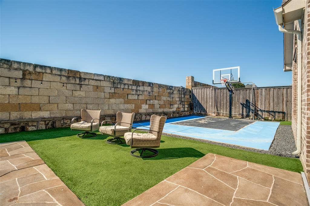 1250 Packsaddle Trail, Prosper, TX 75078 Backyard featuring a stone retaining wall, artificial turf, flagstone-style patio, and a dedicated court with a basketball hoop