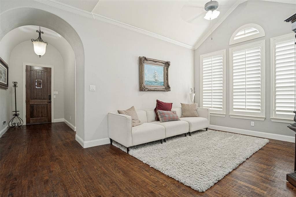 1250 Packsaddle Trail, Prosper, TX 75078 Vaulted ceiling with a ceiling fan, arched doorway, dark wood-finish flooring, and multiple windows with plantation shutters
