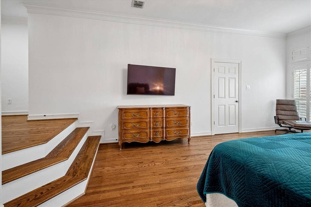 2916 Thomas Avenue, Dallas, TX 75204 Spacious primary bedroom featuring hardwood flooring, wall-mounted flat-screen television, wooden dresser with multiple drawers, and an ensuite bathroom
