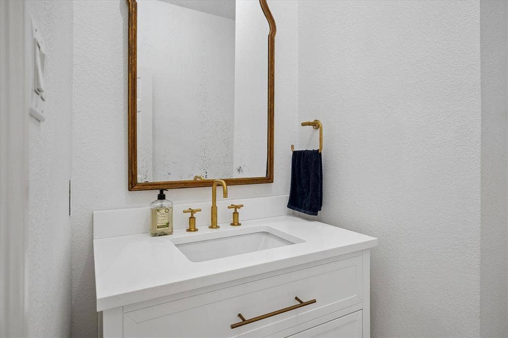 2916 Thomas Avenue, Dallas, TX 75204 Elegant bathroom vanity featuring a white quartz countertop with an integrated rectangular sink, brass-finish three-hole faucet with lever handles, and soft-close cabinetry drawers