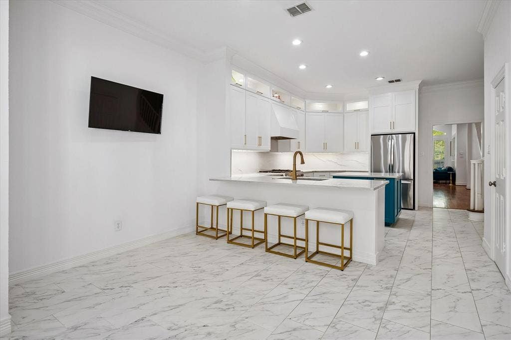 2916 Thomas Avenue, Dallas, TX 75204 White marble-look floor tile, white shaker-style cabinetry, stainless steel refrigerator, white countertops, and a brass-finish faucet