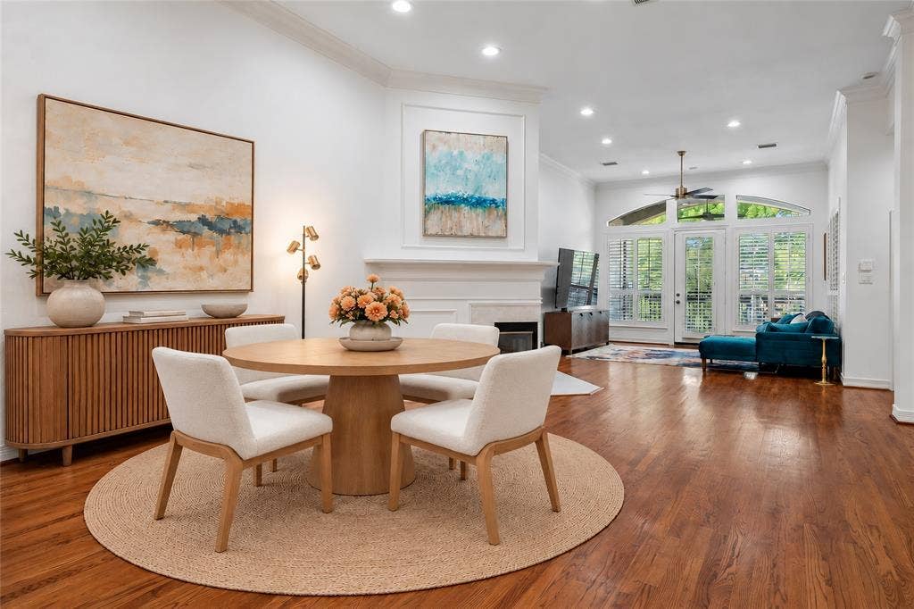 2916 Thomas Avenue, Dallas, TX 75204 Sophisticated open-concept dining and living area featuring warm wood-finish flooring, a round pedestal dining table, cream upholstered chairs, and recessed ceiling lighting