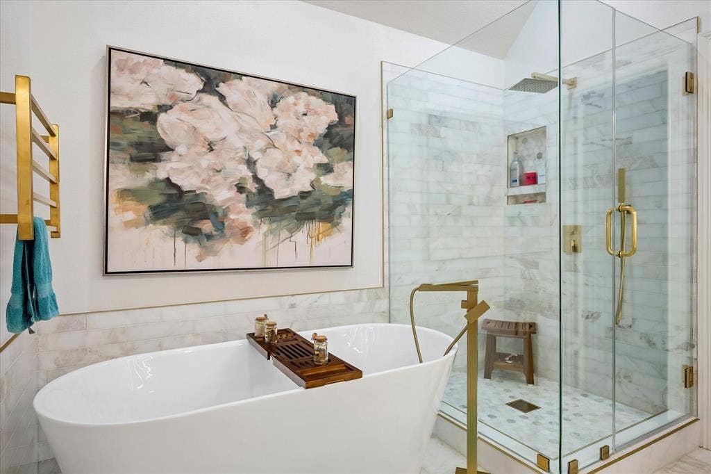 2916 Thomas Avenue, Dallas, TX 75204 Freestanding soaking tub with a floor-mounted gold-tone faucet, glass-enclosed shower with gold-tone fixtures, marble-look subway tile, and a built-in shower niche