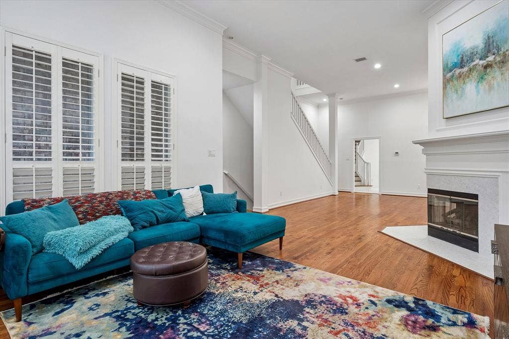 2916 Thomas Avenue, Dallas, TX 75204 Living area featuring wood-finish flooring, a white-mantled fireplace, staircase with white railing, recessed lighting, and tall windows with plantation shutters