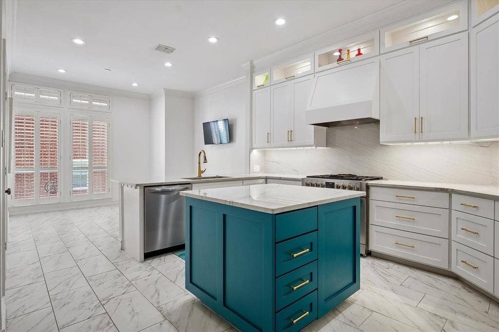 2916 Thomas Avenue, Dallas, TX 75204 Sophisticated kitchen featuring soft-close cabinetry with brushed gold hardware, a striking teal-finished island with multiple drawers, quartz countertops, stainless steel appliances including a gas cooktop, and tile flooring throughout