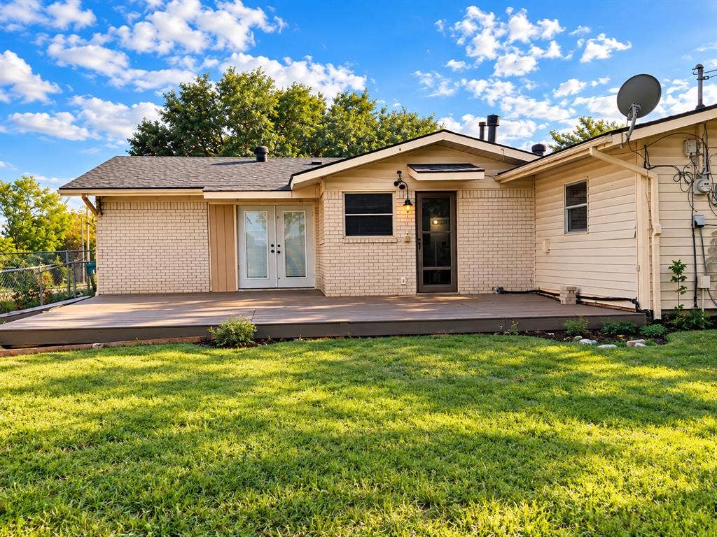 Exterior rear elevation featuring light-toned brick and horizontal siding, a composite deck, double-door entry, and a screened door with integrated hardware