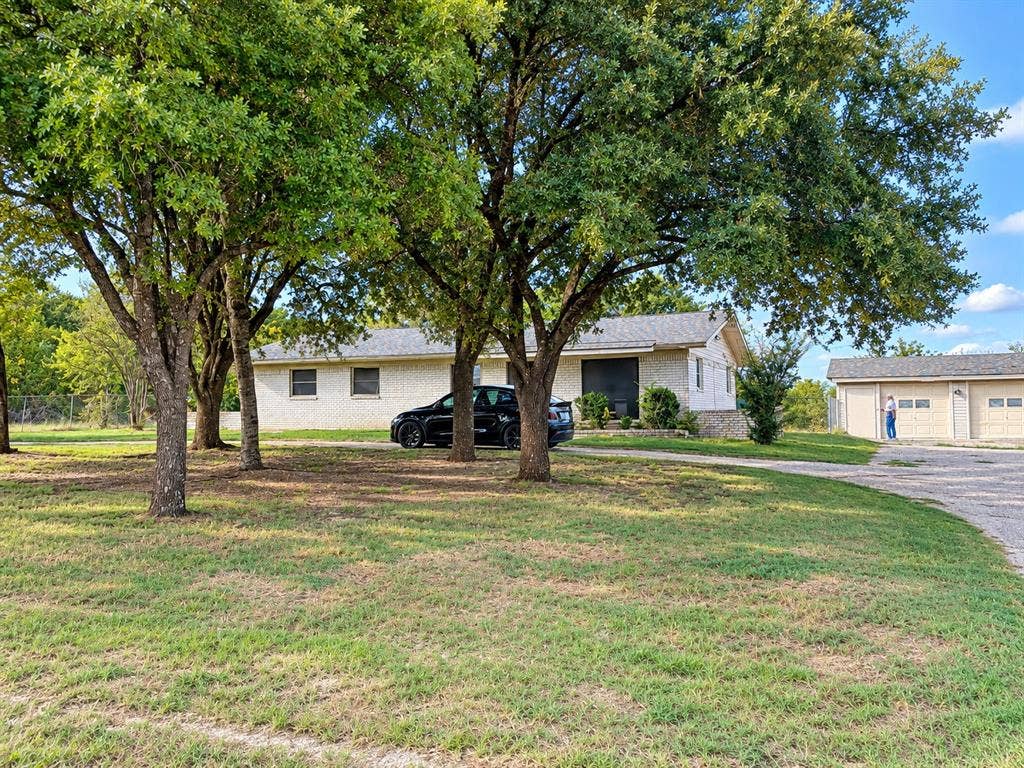 Single-story brick exterior residence featuring a detached two-car garage and mature trees on a spacious lot