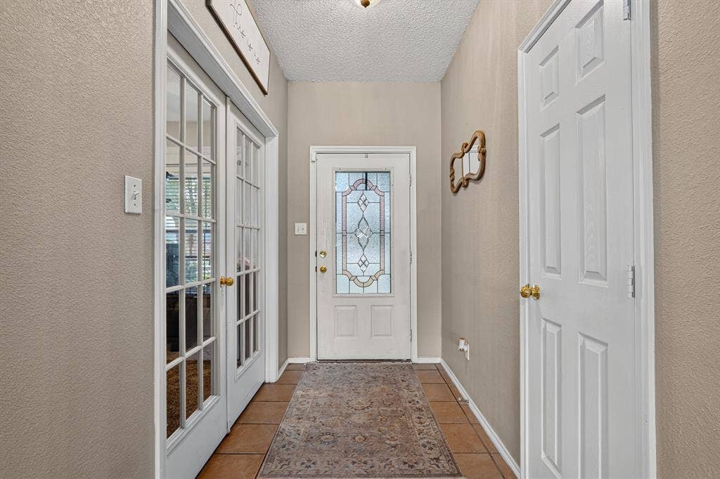 Entryway featuring a decorative glass panel front door, durable tile flooring, and white French doors