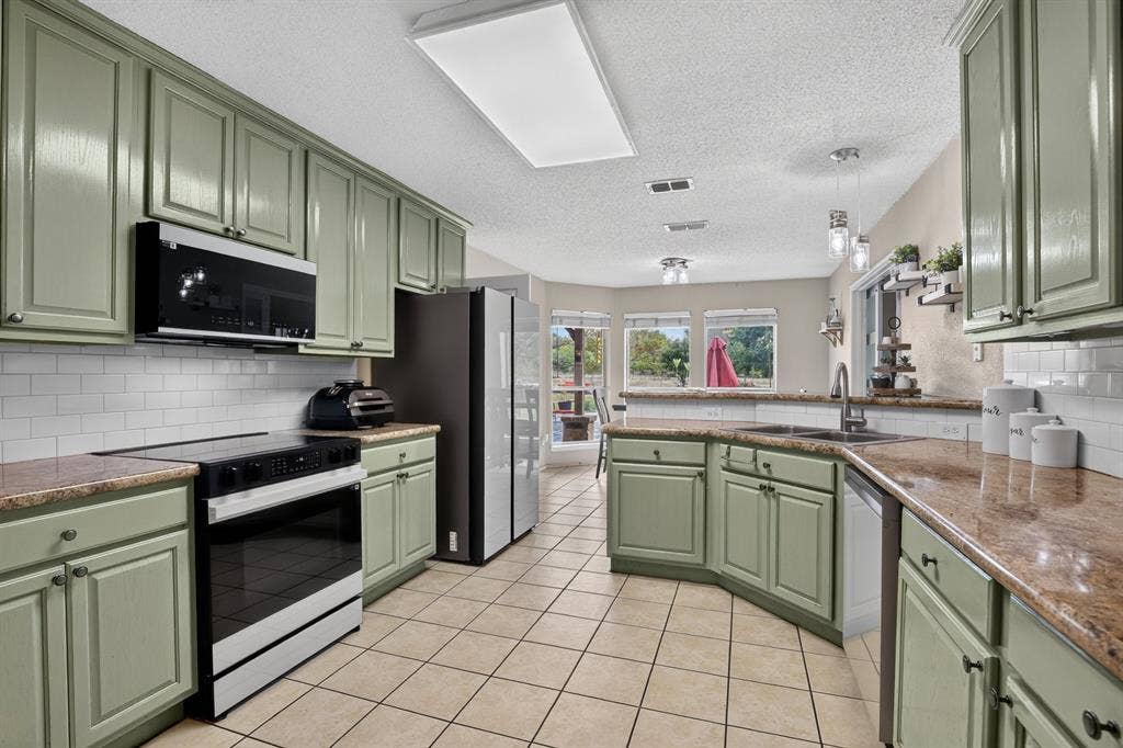 Kitchen featuring sage cabinetry, tile flooring, granite countertops, subway tile backsplash, and stainless steel appliances