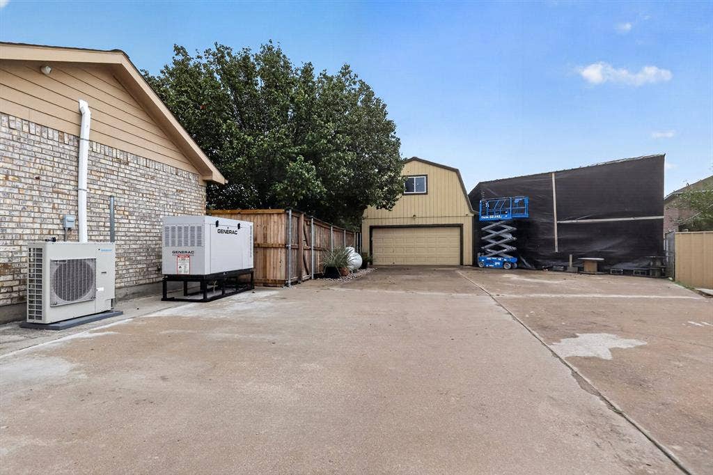 Brick exterior with vinyl siding, concrete driveway, wood privacy fence, detached garage with gambrel roof, and whole-house generator