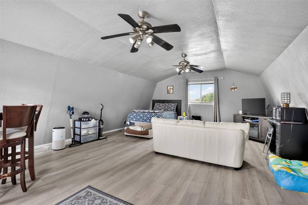 Vaulted ceiling, ceiling fans, wood-finish flooring, window with natural light, and a built-in bar-height counter
