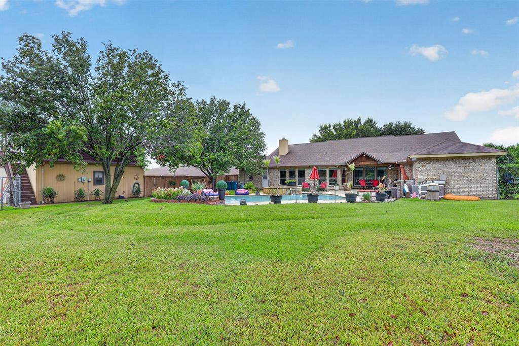 Expansive green lawn leading to a brick-clad residence with a pitched shingle roof, outdoor swimming pool, and a dedicated patio area