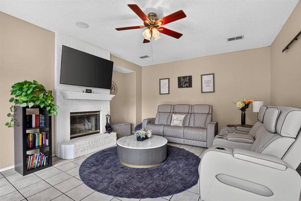 White brick fireplace with a mantel, mounted television, wood-finish ceiling fan, recessed lighting, and tile flooring