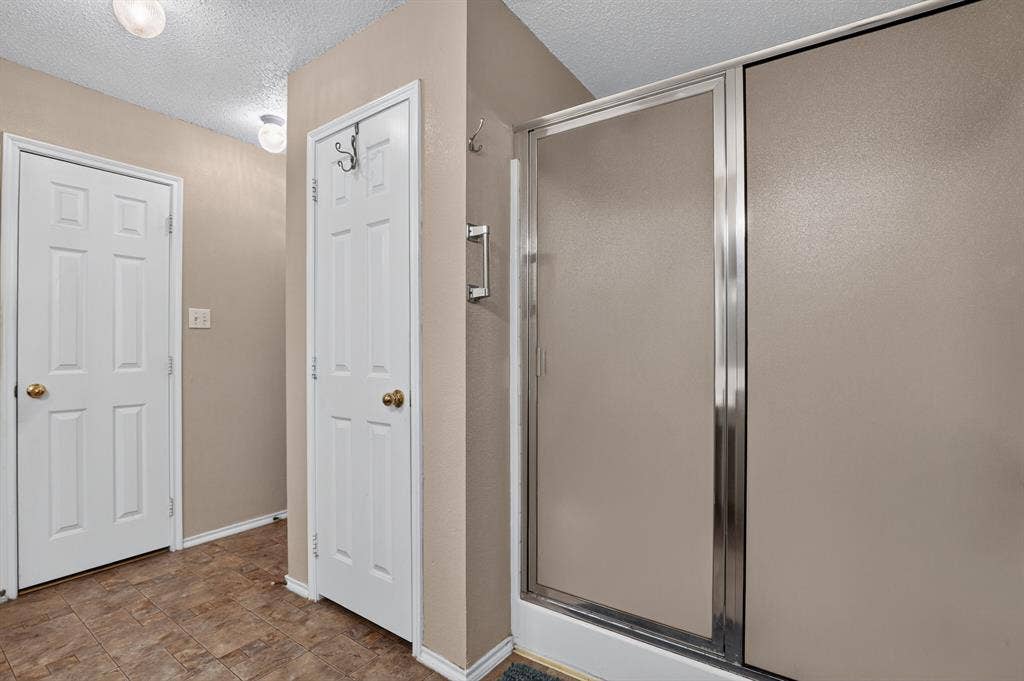 Enclosed shower with frosted glass doors, white six-panel doors with brass hardware, and wood-finish flooring