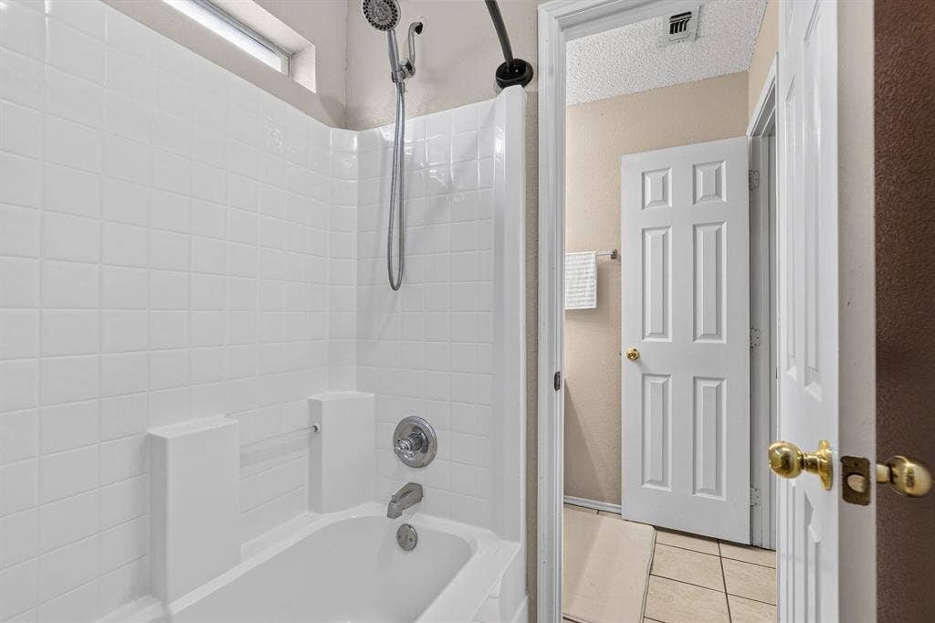 White tiled shower surround with chrome fixtures, a combination showerhead and handheld sprayer, and a small transom window
