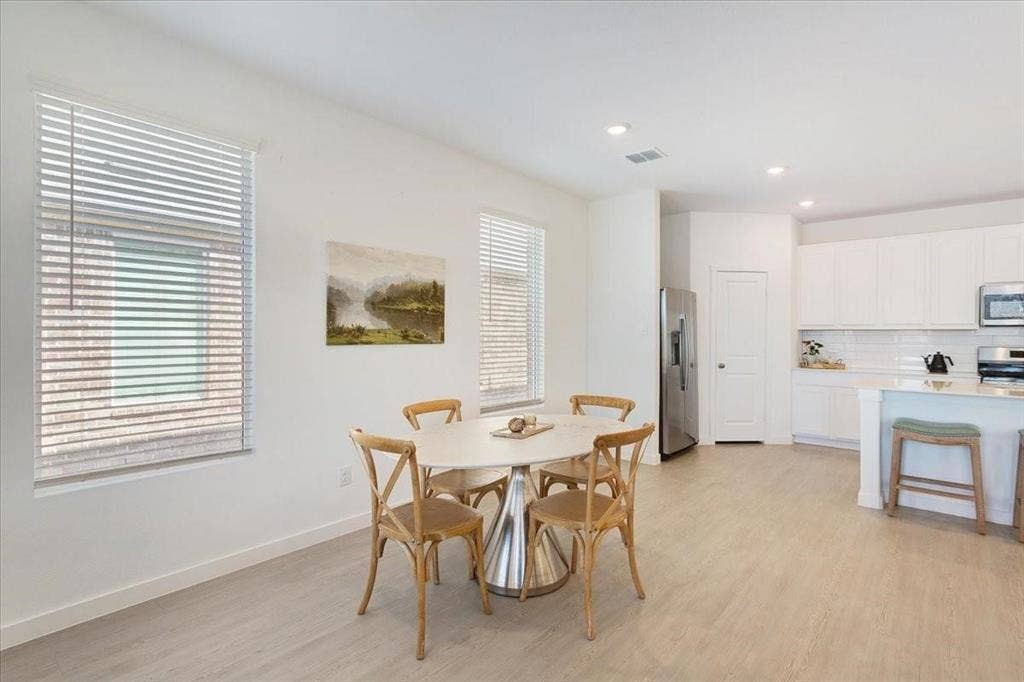Open-concept kitchen and dining area featuring light wood-finish flooring, white cabinetry, stainless steel appliances, and recessed lighting