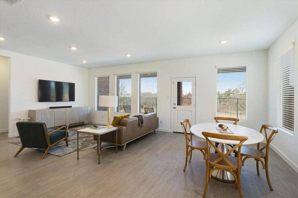 Recessed lighting, wood-finish flooring, multiple windows with blinds, a built-in media console, and a white exterior door