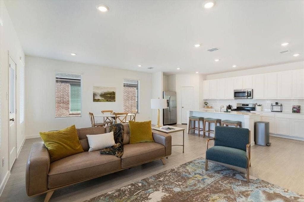 Open-concept living space featuring wood-finish flooring, recessed lighting, and a kitchen with white cabinetry, stainless steel appliances, and a central island with seating