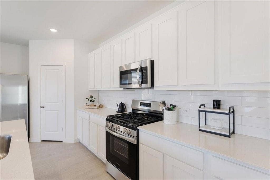 Contemporary kitchen with white shaker-style cabinetry, stainless steel appliances, light-toned countertops, and subway tile backsplash