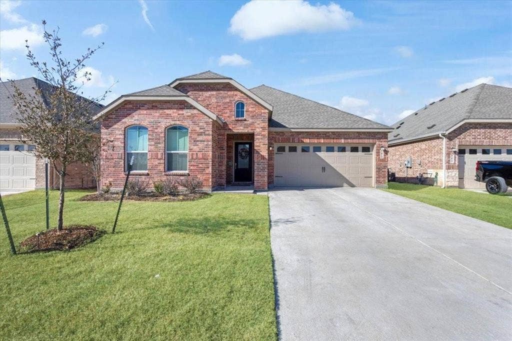 Red brick exterior with arched windows, an attached two-car garage, concrete driveway, and front lawn