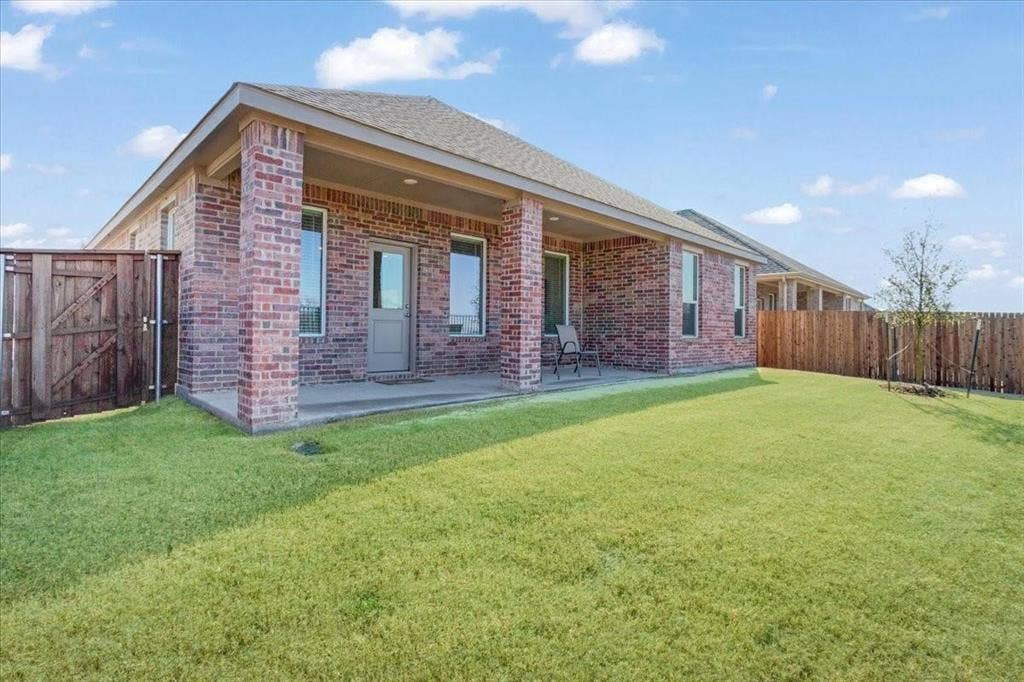 Expansive backyard featuring a covered patio, red brick exterior, multiple windows, and a wood privacy fence