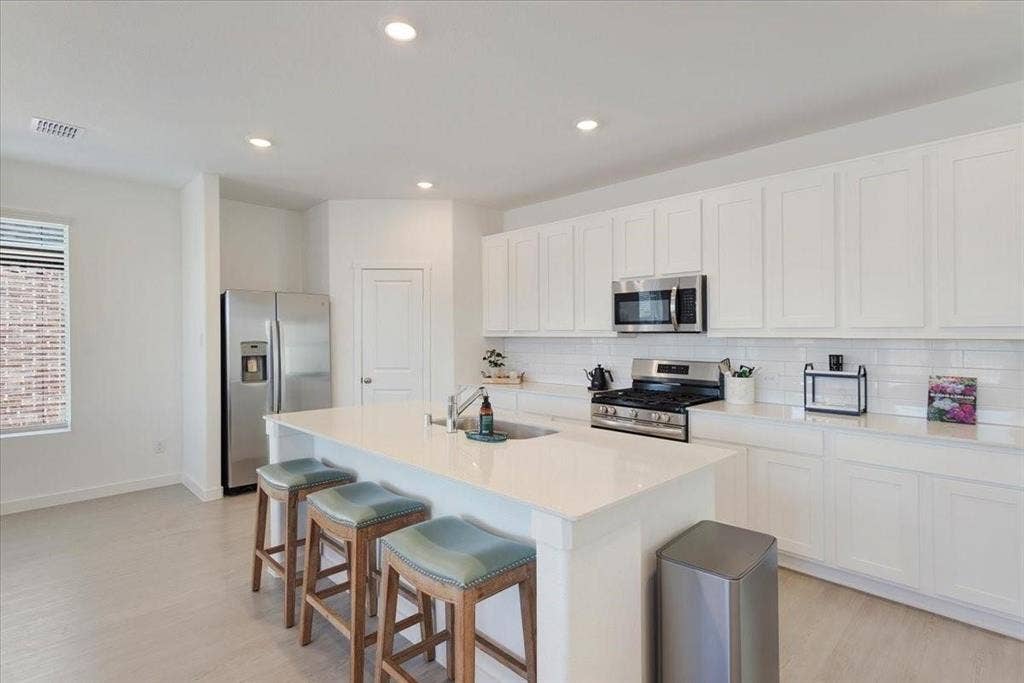Contemporary kitchen featuring white shaker cabinetry, stainless steel appliances, a large center island with seating, recessed lighting, and light wood-finish flooring