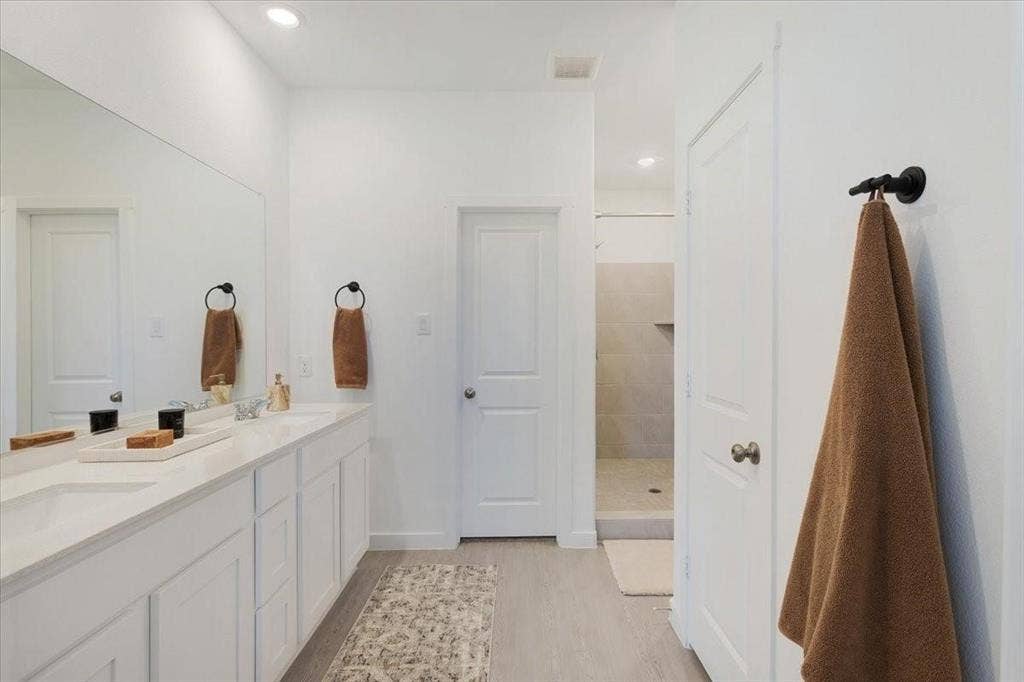 Dual vanity with integrated sinks, expansive mirror, recessed lighting, and a tiled shower stall