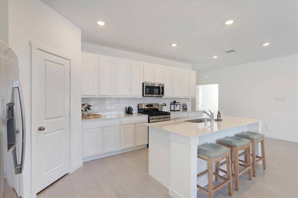 Kitchen featuring white cabinetry, subway tile backsplash, stainless steel appliances, an island with an undermount sink, and recessed lighting