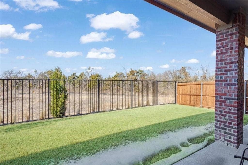 Covered patio with a brick column, concrete flooring, and an artificial turf lawn