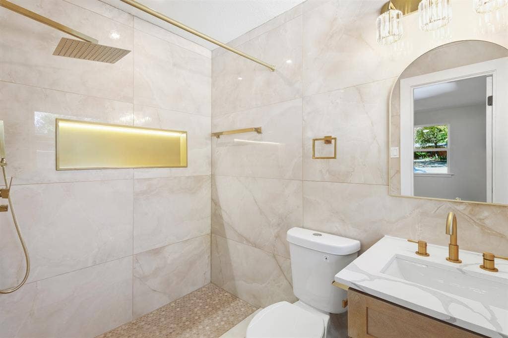 917 Blossom Circle, Garland, TX 75041 master bathroom featuring wall to wall tile shower with a gold-toned niche, a rain shower head, and a pebble-tiled floor