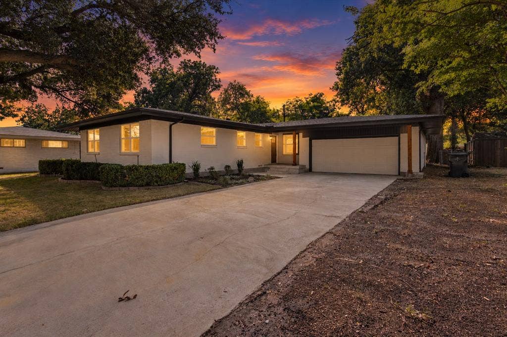 917 Blossom Circle, Garland, TX 75041 White exterior with dark trim, attached garage with white door, concrete driveway, and mature landscaping