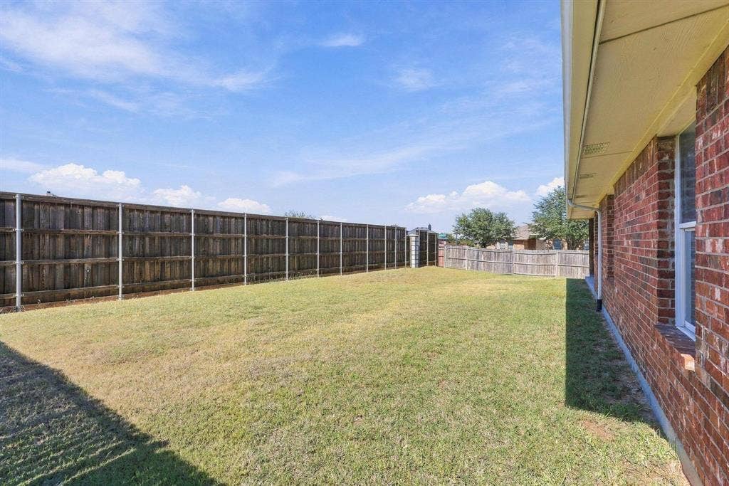 Expansive backyard with a manicured lawn, full wood privacy fencing, and a brick exterior