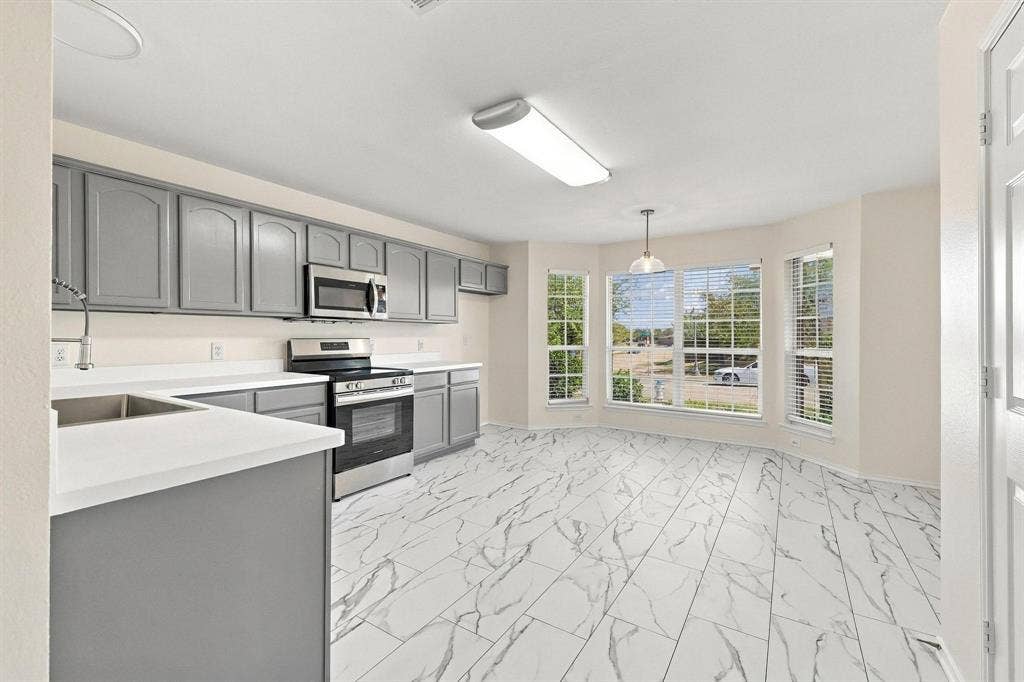 Kitchen featuring gray cabinetry, stainless steel appliances, white countertops, and marble-look tile flooring