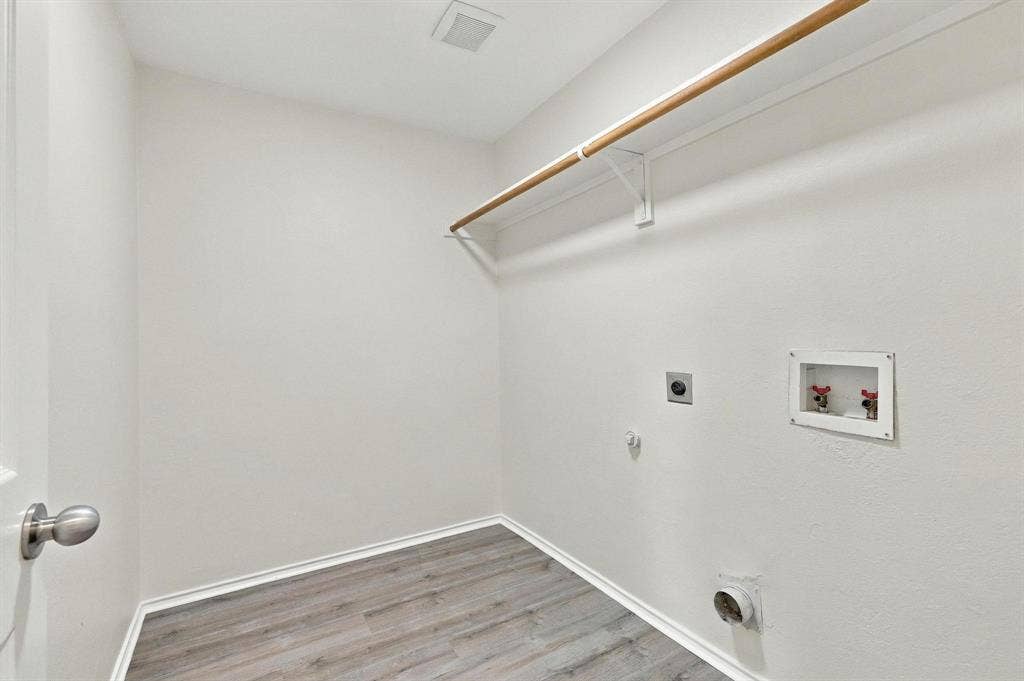 Laundry area featuring wood-finish flooring, a wall-mounted clothing rod, and visible utility connections