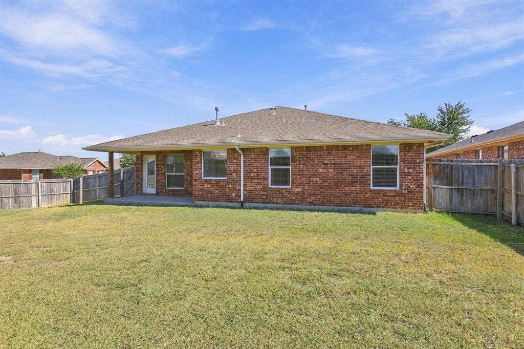 Expansive backyard with a manicured lawn, full brick exterior, and a covered patio area