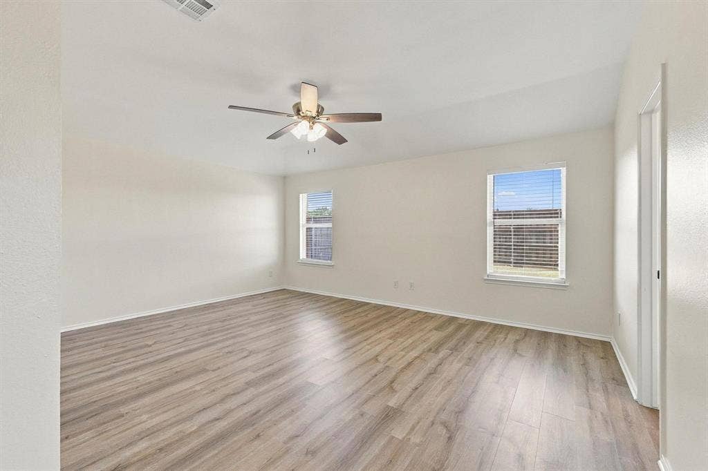 Spacious room featuring wood-finish flooring, two windows with blinds, and a ceiling fan