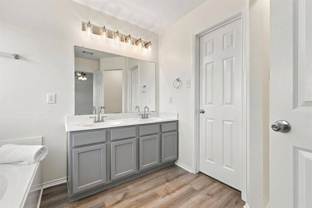 Dual vanity with gray cabinetry, white countertops, dual undermount sinks, and wood-finish flooring