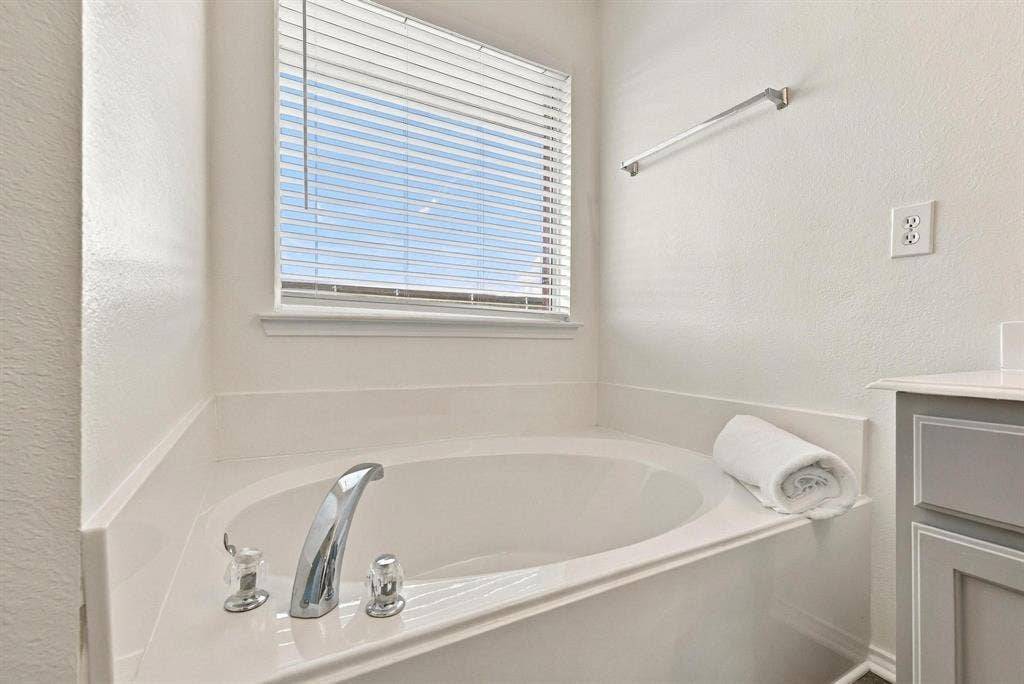 Alcove soaking tub with chrome fixtures, integrated white countertop, and window with horizontal blinds