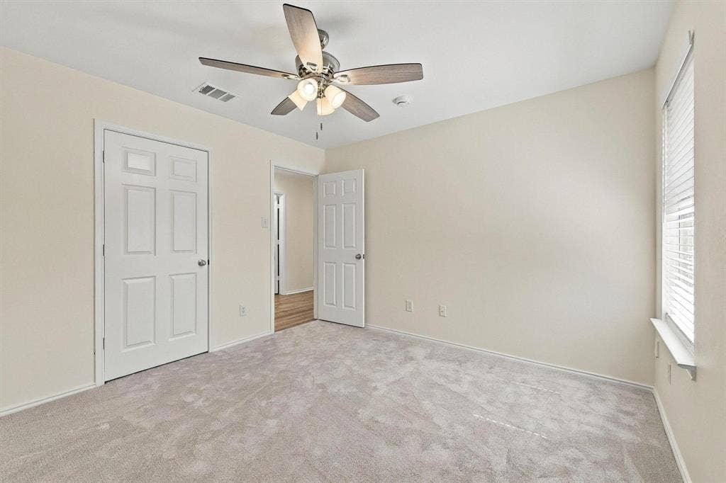 Carpeted room with a ceiling fan, paneled doors, and a window with blinds