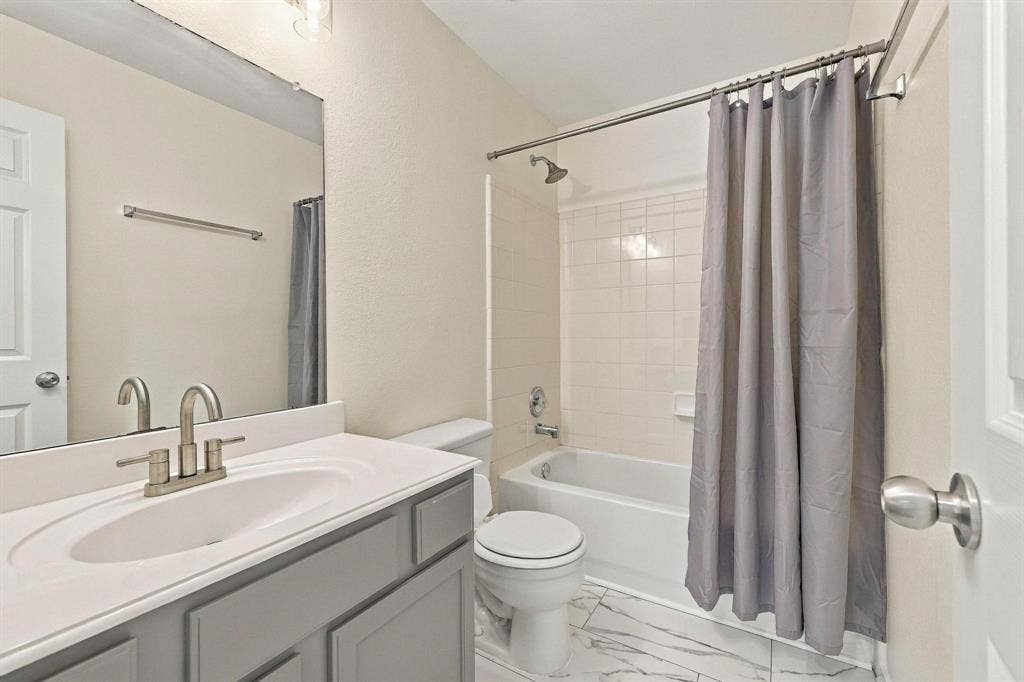 Bathroom featuring a vanity with an integrated sink, brushed nickel faucet, light-colored cabinetry, a bathtub with a tiled surround, and patterned floor tiling