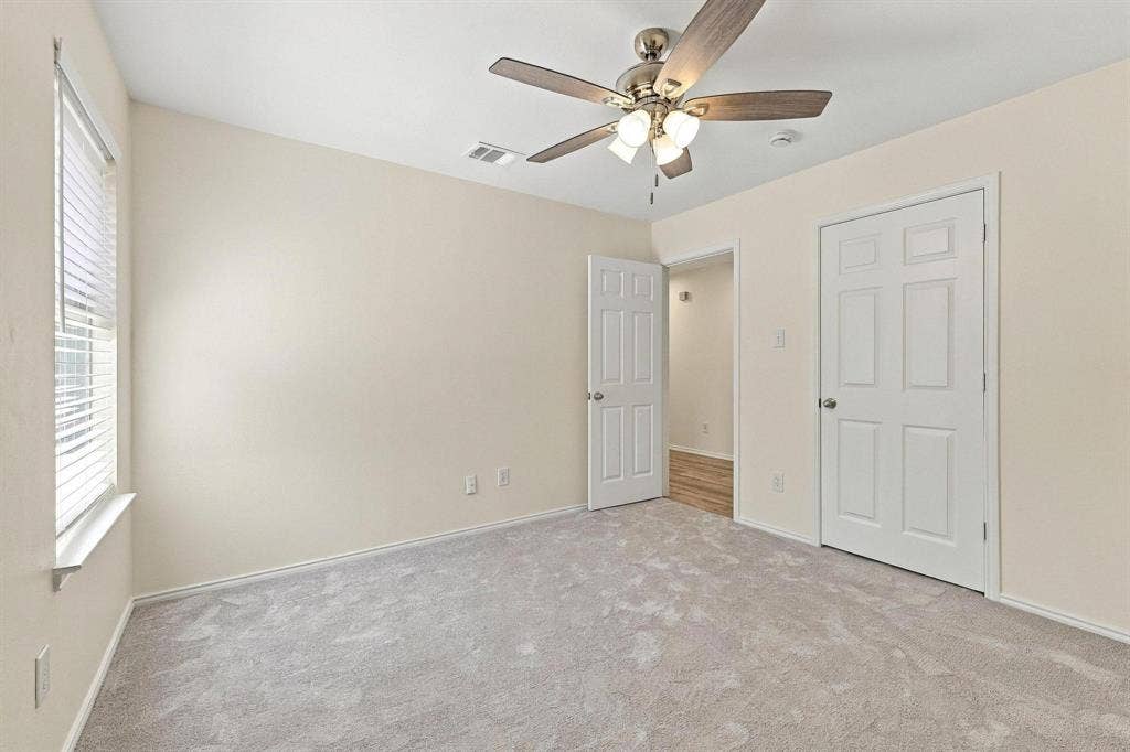 Plush carpet flooring, neutral paint palette, ceiling fan with integrated lighting, white paneled doors, and window with blinds