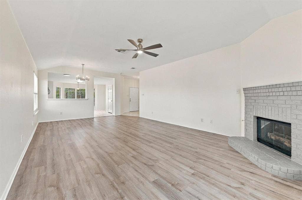 Vaulted ceilings, wood-finish flooring, a brick fireplace, and a ceiling fan with integrated lighting