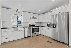 Modern kitchen featuring white cabinetry, dark countertops, a stainless steel farmhouse sink, and stainless steel appliances