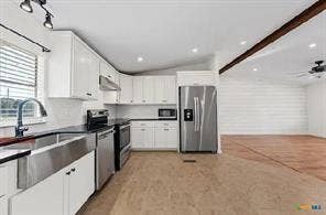 Modern kitchen with white cabinetry, stainless steel appliances, a large farmhouse sink, and dark countertops