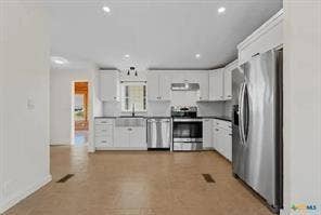 Kitchen featuring white cabinetry, dark countertops, stainless steel appliances, and wood-finish flooring