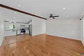Hardwood flooring, exposed ceiling beam, recessed lighting, white shiplap accent wall, and stainless steel kitchen appliances