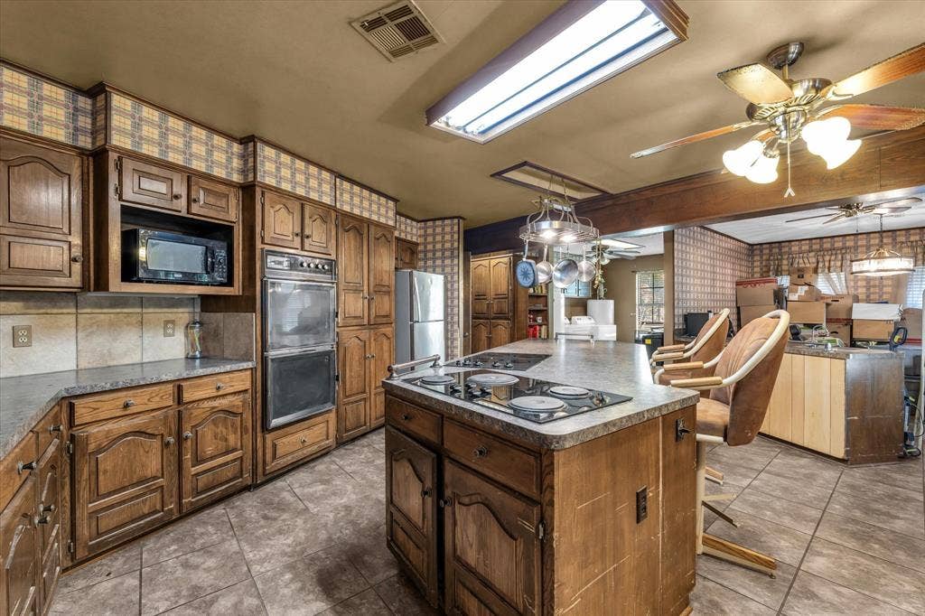 4201 N 19th Street, Waco, TX 76708 Kitchen featuring wood cabinetry, an integrated double oven, a center island with a cooktop, and tile flooring