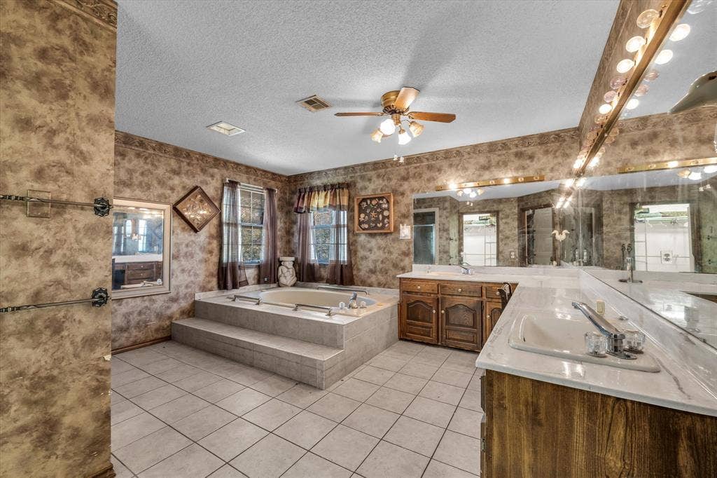 4201 N 19th Street, Waco, TX 76708 Tile flooring, built-in soaking tub with tiled surround, dual vanity with undermount sinks, wood-finish cabinetry, and mirrored wall with integrated lighting