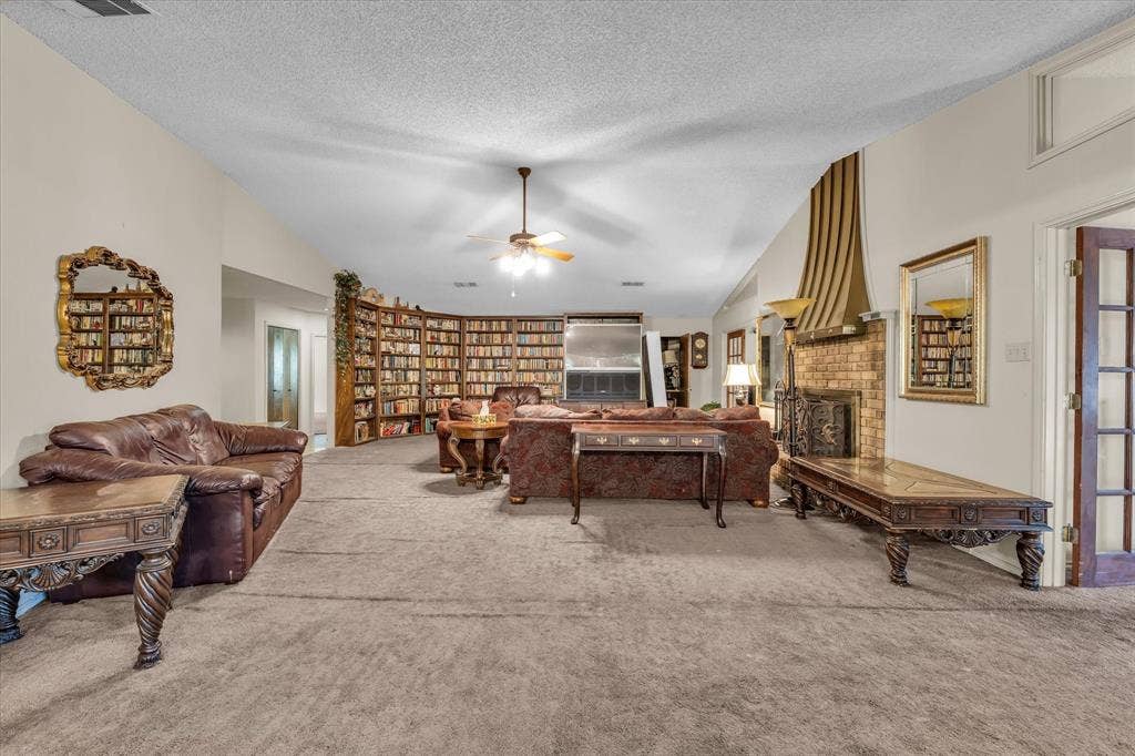 4201 N 19th Street, Waco, TX 76708 Vaulted ceilings, a built-in curved bookshelf, a brick fireplace with a decorative mantel, and a ceiling fan create a spacious interior